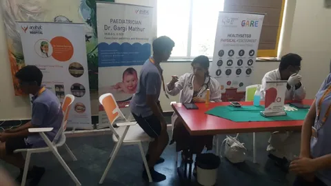 Dr Gargi Mathur, wearing a stethoscope, seated at a table examining a schoolchild during a school health assessment camp.
